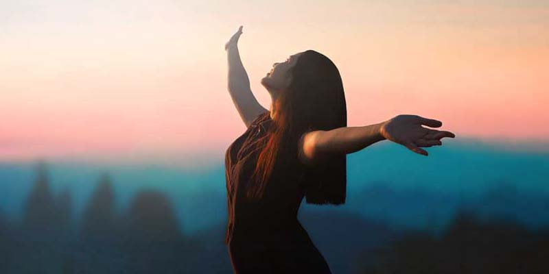 Happy woman raised hand on blurred mountain sunrise background.
