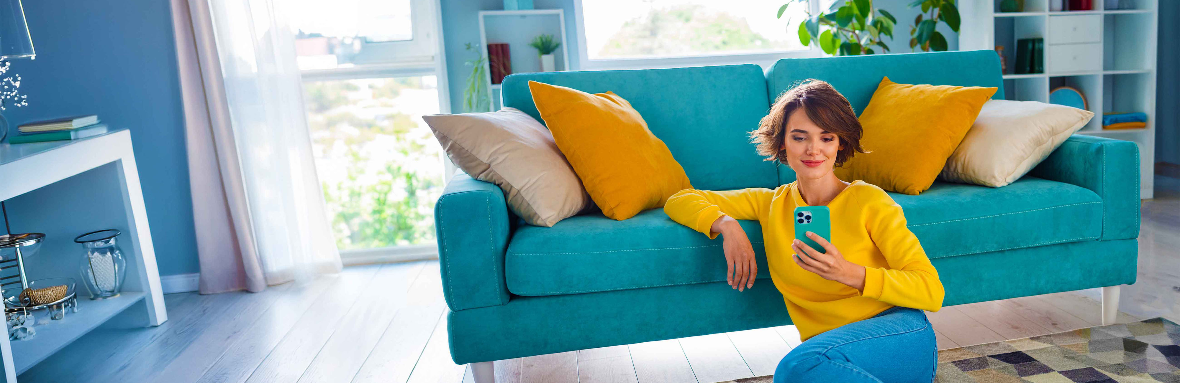 Woman sitting on the floor, leaning on the couch looking at her phone