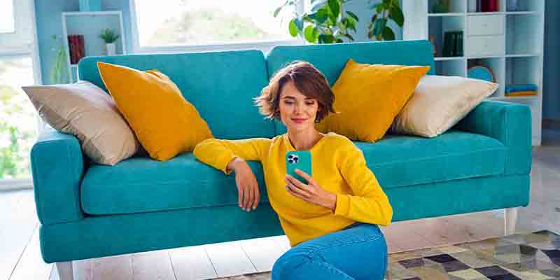 Woman sitting on the floor, leaning on the couch looking at her phone